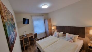 A hotel room with a bed, bedside tables, a desk, a chair, a television, and a window with curtains.