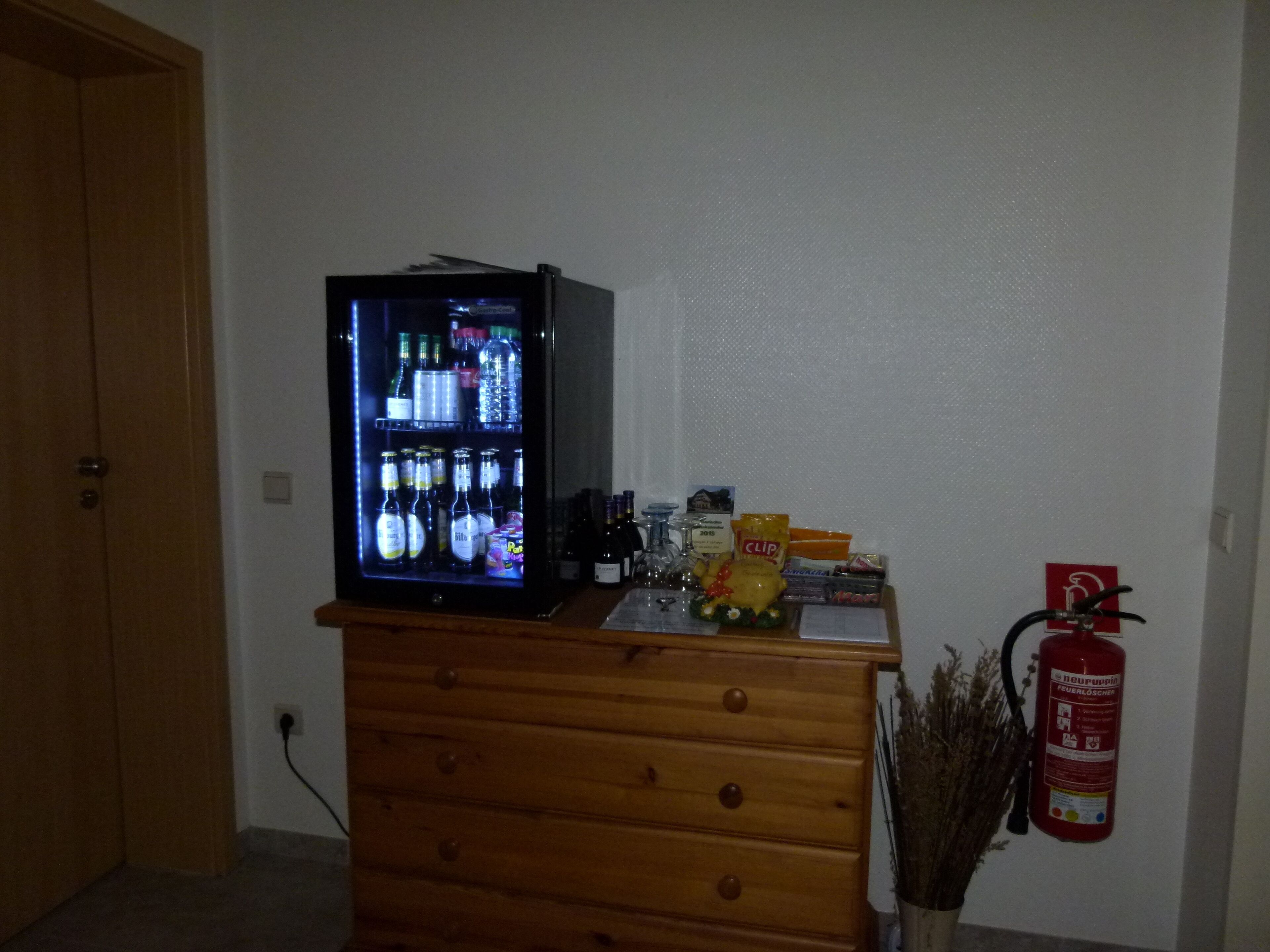 A room with a wooden dresser, a television on top, a fire extinguisher, and a wall socket.