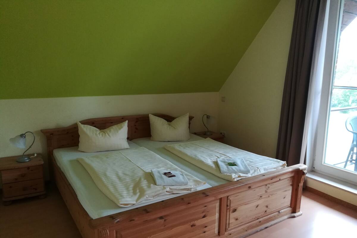 Quarto com cama de madeira, duas mesinhas de cabeceira e uma janela com cortinas.