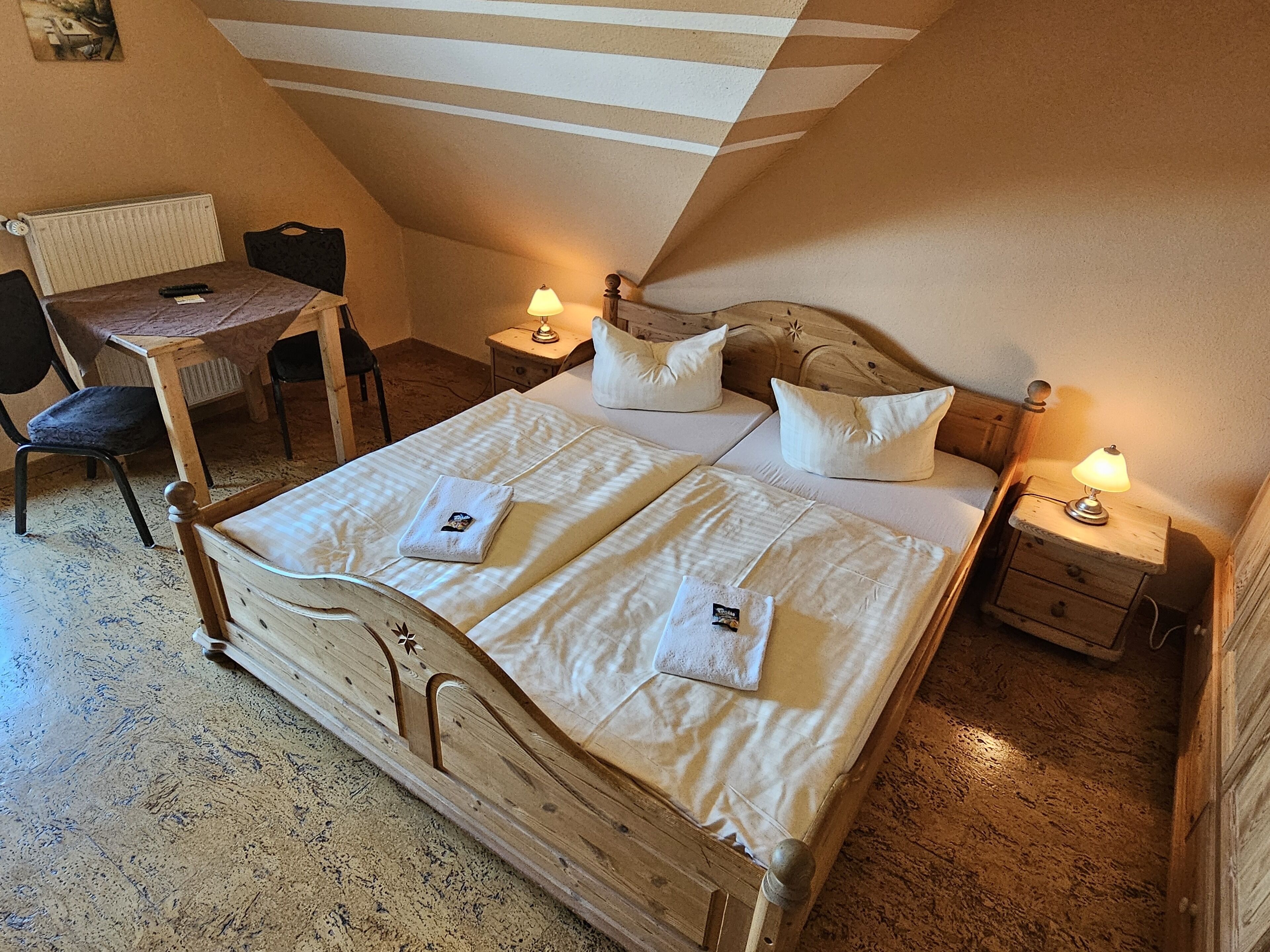 Um quarto com uma cama de madeira, duas mesas de cabeceira com luminárias, uma cadeira e uma pequena mesa.