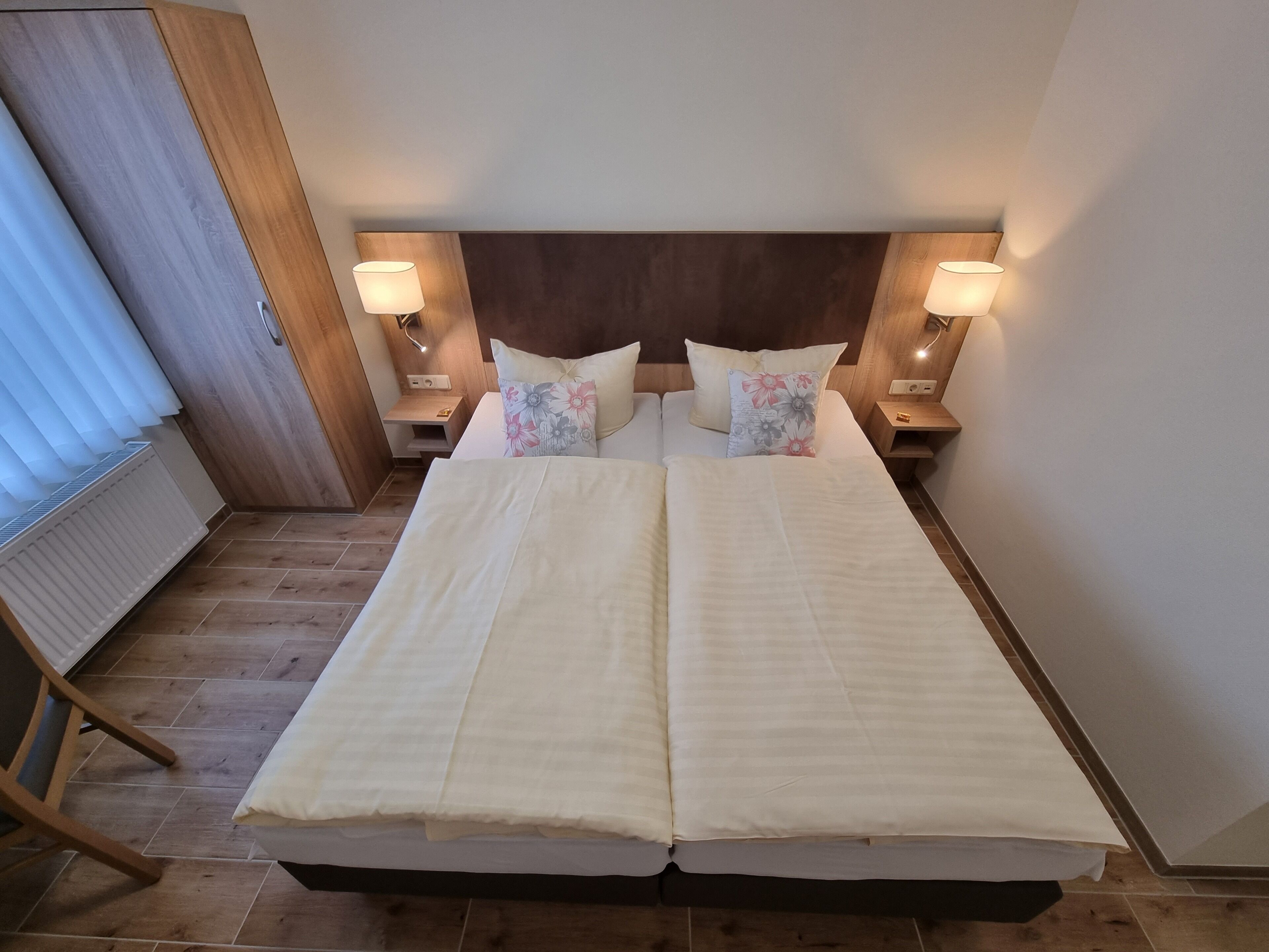 Cama doble con cabecera de madera, dos mesitas de noche con lámparas y un radiador en el suelo.