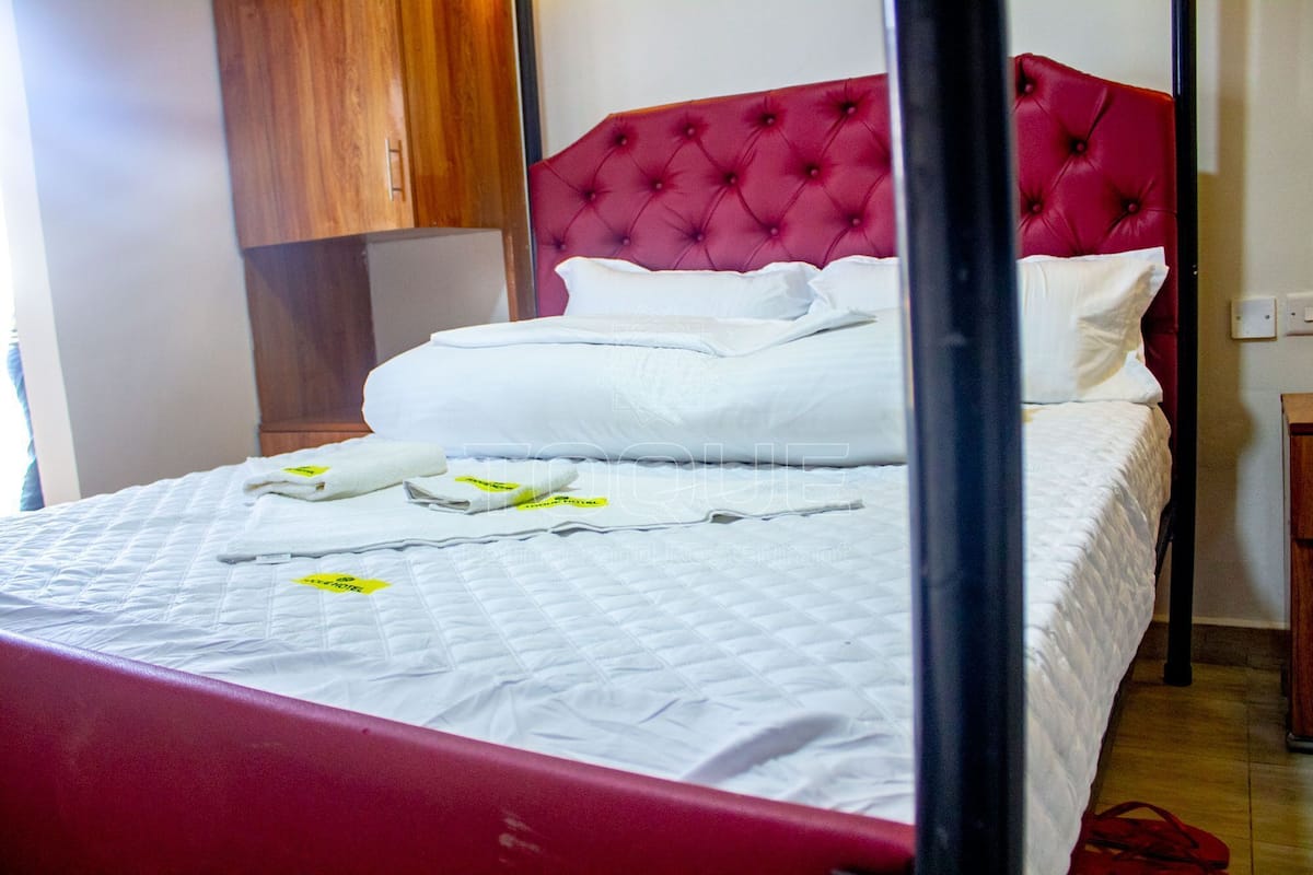 A bed with white bedding, a red headboard, and a wooden wardrobe in the background.