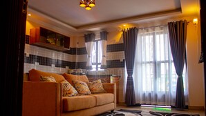 A living room with a sofa, patterned rug, and a kitchen area with tiled backsplash and cabinets. - Toque Hotel (Nairobi)