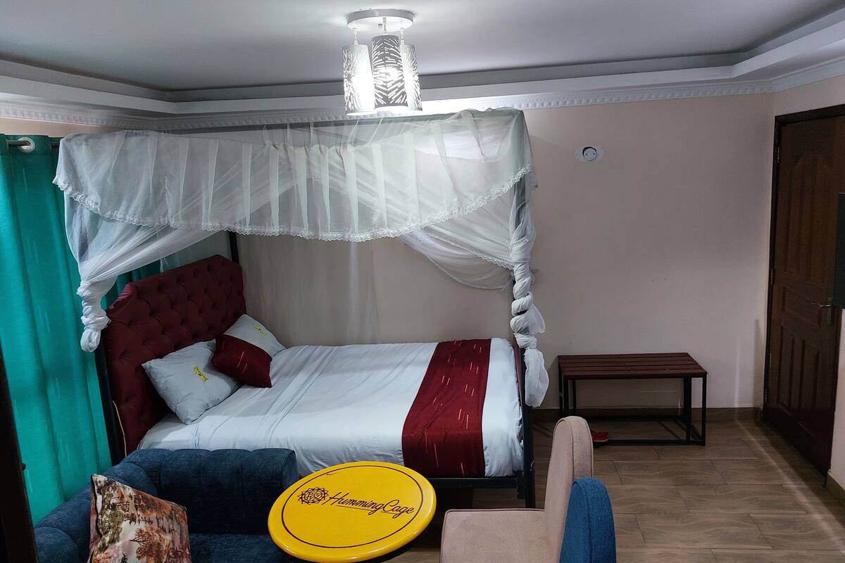 A bedroom with a bed, a bedside table, a chair, a bedside lamp, and a window with curtains.