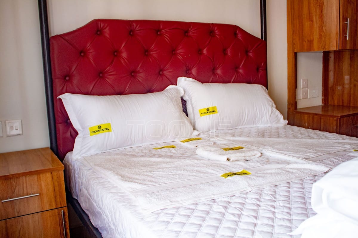 A hotel room with a red tufted headboard, white bedding, and a wooden nightstand.