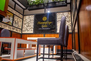 A hotel interior with a reception desk, a seating area with a chair, and a wall with a logo for 'Humming Cage Suites'.