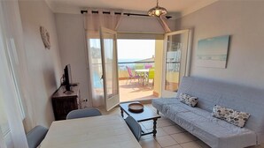 Una sala de estar con sofá, una mesa de comedor y sillas. Cuenta con un balcón con vistas al mar.