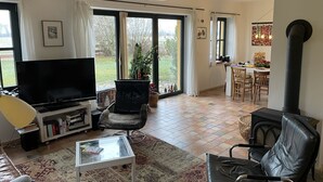 Een woonkamer met een televisie, leren fauteuils, een glazen salontafel en een open haard.