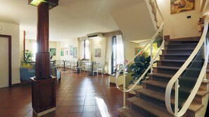 A spacious lobby with a staircase, a wooden column, and a dining area. - Hotel Arcobaleno Siena (Siena)