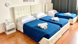 A hotel room with two beds, each with a blue bedspread and white pillows. There is a small bedside table with a phone and a power outlet. A painting of a cityscape is on the wall above the beds. - Oasi San Francesco (Rome)