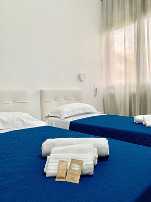 A hotel room with two beds, each with a blue bedspread and white pillows. There are towels and two small bottles on the beds. - Oasi San Francesco (Rome)