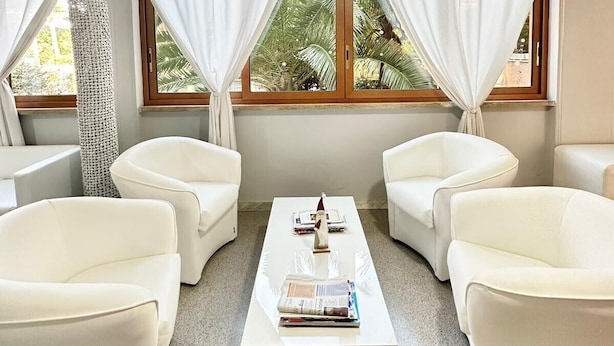 A room with two white sofas, a central coffee table, and large windows with white curtains. - Oasi San Francesco (Rome)