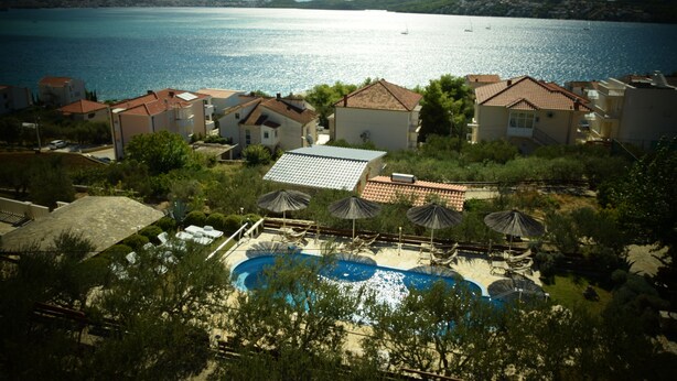 A resort with a swimming pool, umbrellas, and a view of the sea. - Villa Julio's  fully separate stone house , located in the middle of garden (Seget Donji)