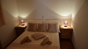 A neatly made bed with a patterned bedspread, two bedside lamps, and a wooden nightstand. - Villa Julio's  fully separate stone house , located in the middle of garden (Seget Donji)