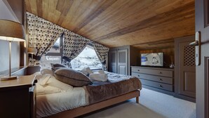 Un dormitorio con techo de madera, una cama con almohadas, un televisor en una cómoda y una ventana con cortinas.