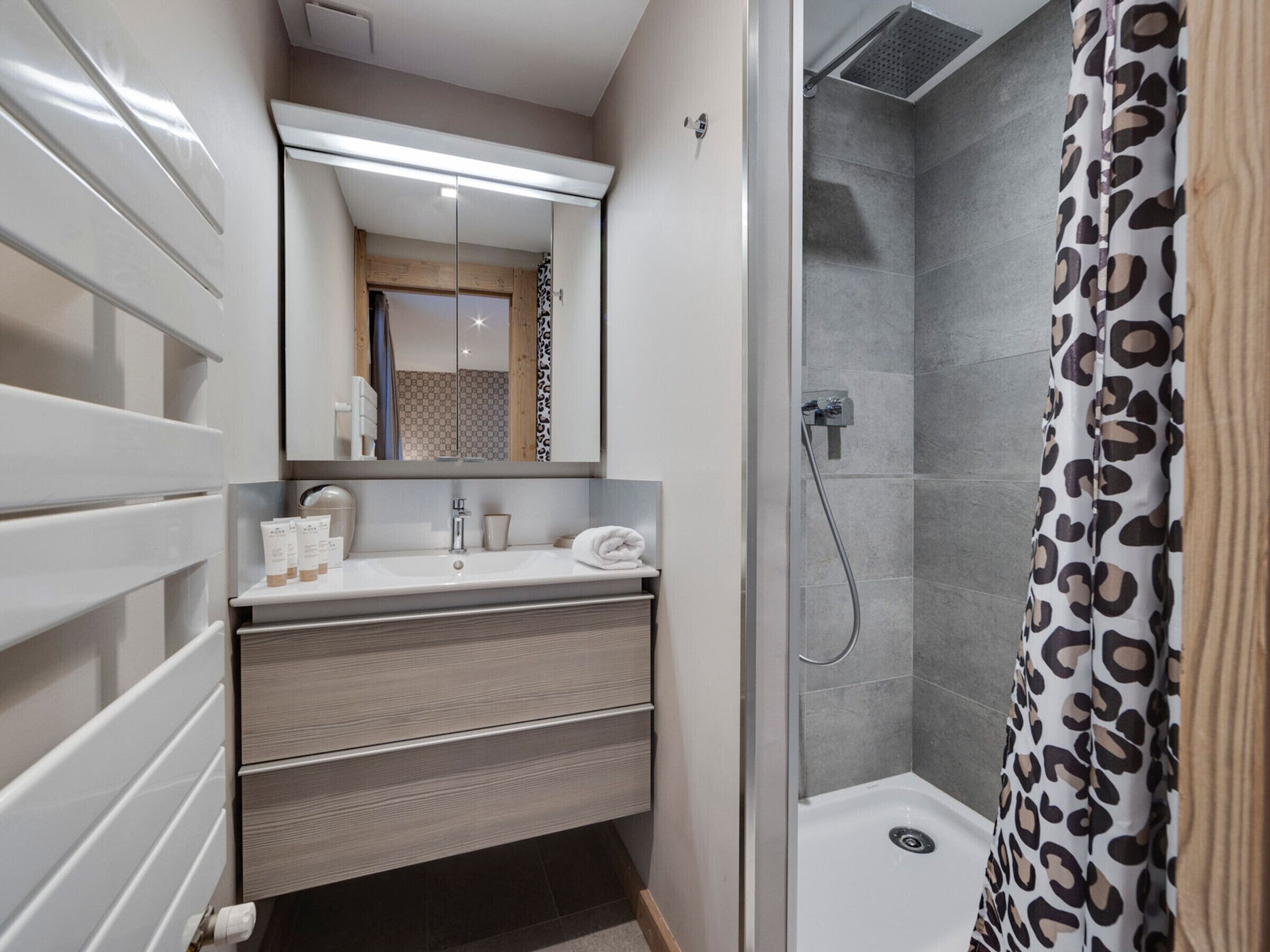 A modern bathroom with a shower, a vanity with a mirror, and a towel rack.