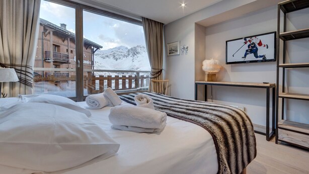 Habitación de hotel con cama, ventana con vistas a montañas, televisión y estante con lámpara.