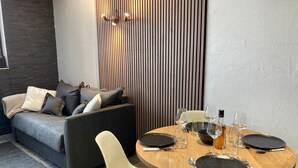 A modern living room with a grey sofa, a wooden dining table set with plates, glasses, and cutlery, and a white chair.