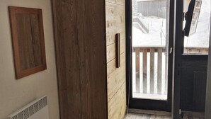 A room with a wooden wardrobe, a vent, and a sliding glass door leading to a balcony with a view of a snowy outdoor area.