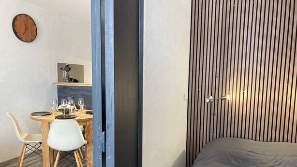 A modern room with a bed, a dining area with a table and chairs, and a kitchen area.