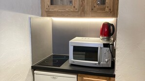 A compact kitchen with a microwave, a kettle, and a small refrigerator.