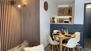 A modern living room with a wooden accent wall, a dining area with a round table and chairs, and a kitchen in the background.