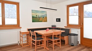 Ein gemütliches Zimmer mit Holztisch und -stühlen, einer Bank, einem Heizkörper, einem Mülleimer und einem Bild an der Wand.