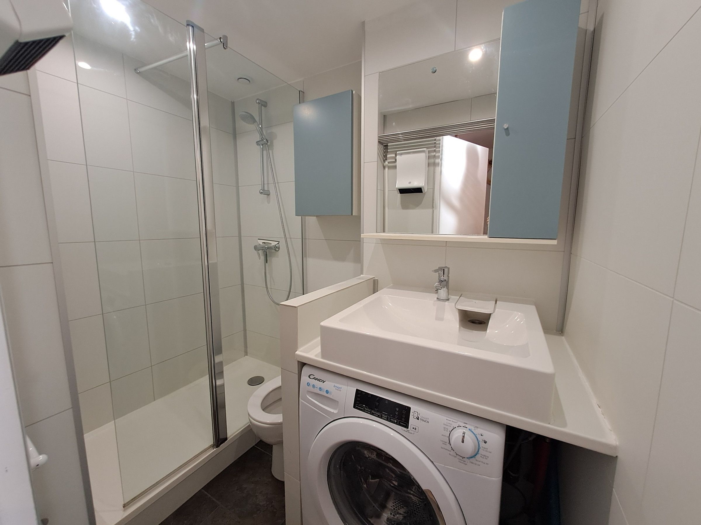 Une salle de bain avec une douche à parois de verre, des toilettes, un lave-linge et un lavabo avec un miroir au-dessus.