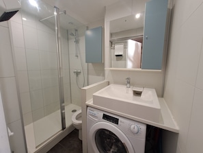 Bagno con doccia vetrata, un WC, una lavatrice e un lavandino con uno specchio sopra.