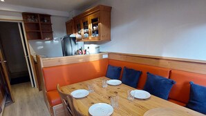 Un espace repas avec une table en bois, un banc rembourré de coussins orange et des placards en bois au-dessus.