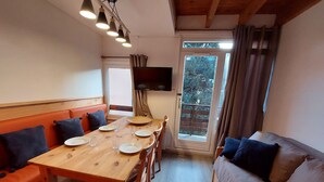 Un coin repas avec une table en bois dressée pour quatre personnes, entourée de bancs rembourrés de coussins orange.