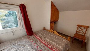 Une chambre à coucher avec un lit, une chaise en bois, une fenêtre avec un rideau rouge et une armoire en bois.