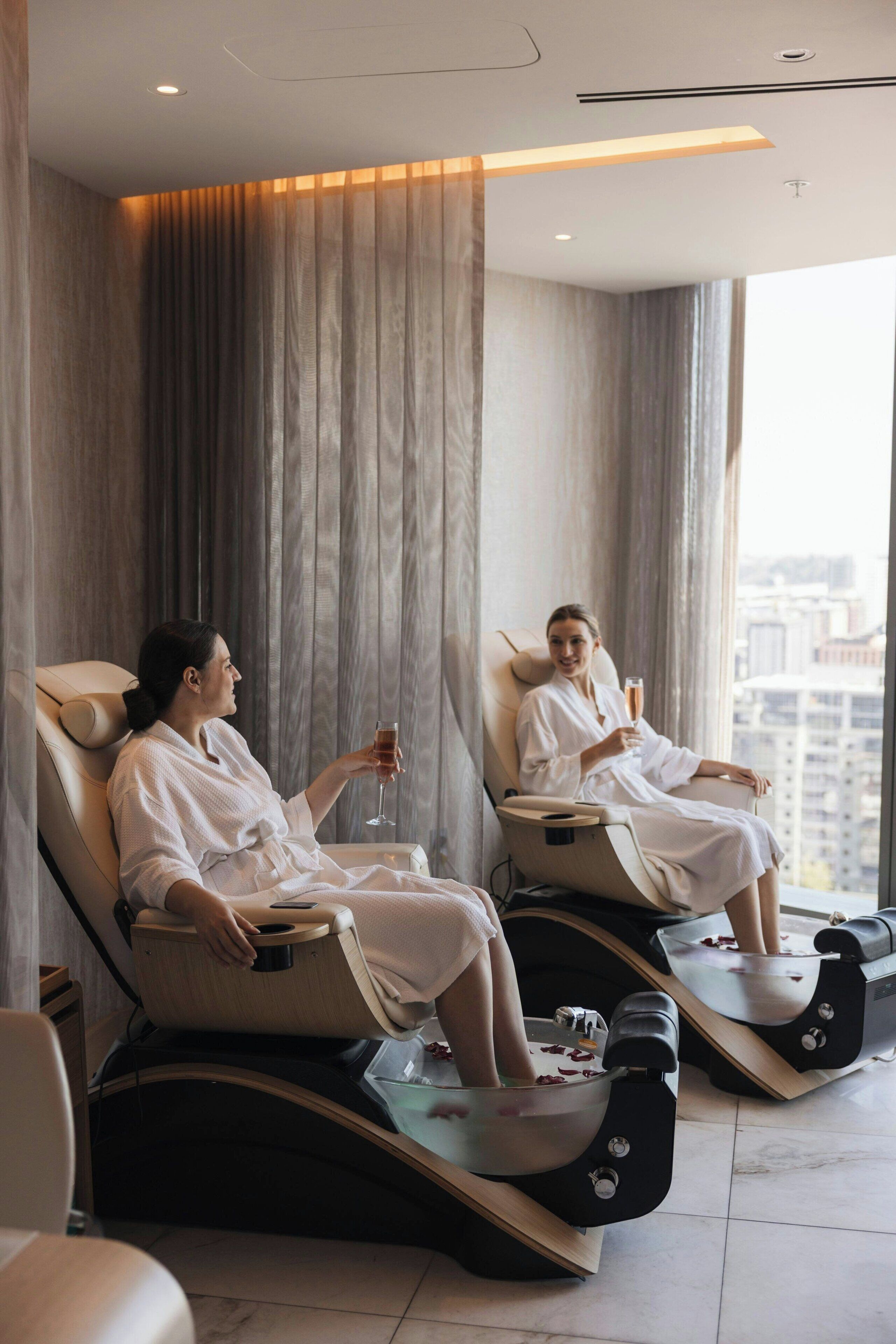 Two massage chairs in a room with large windows and curtains.