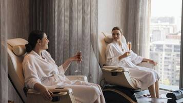 Two massage chairs in a room with large windows and curtains.