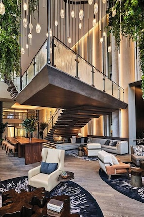 A spacious lobby with a central staircase, seating areas, and hanging light fixtures.