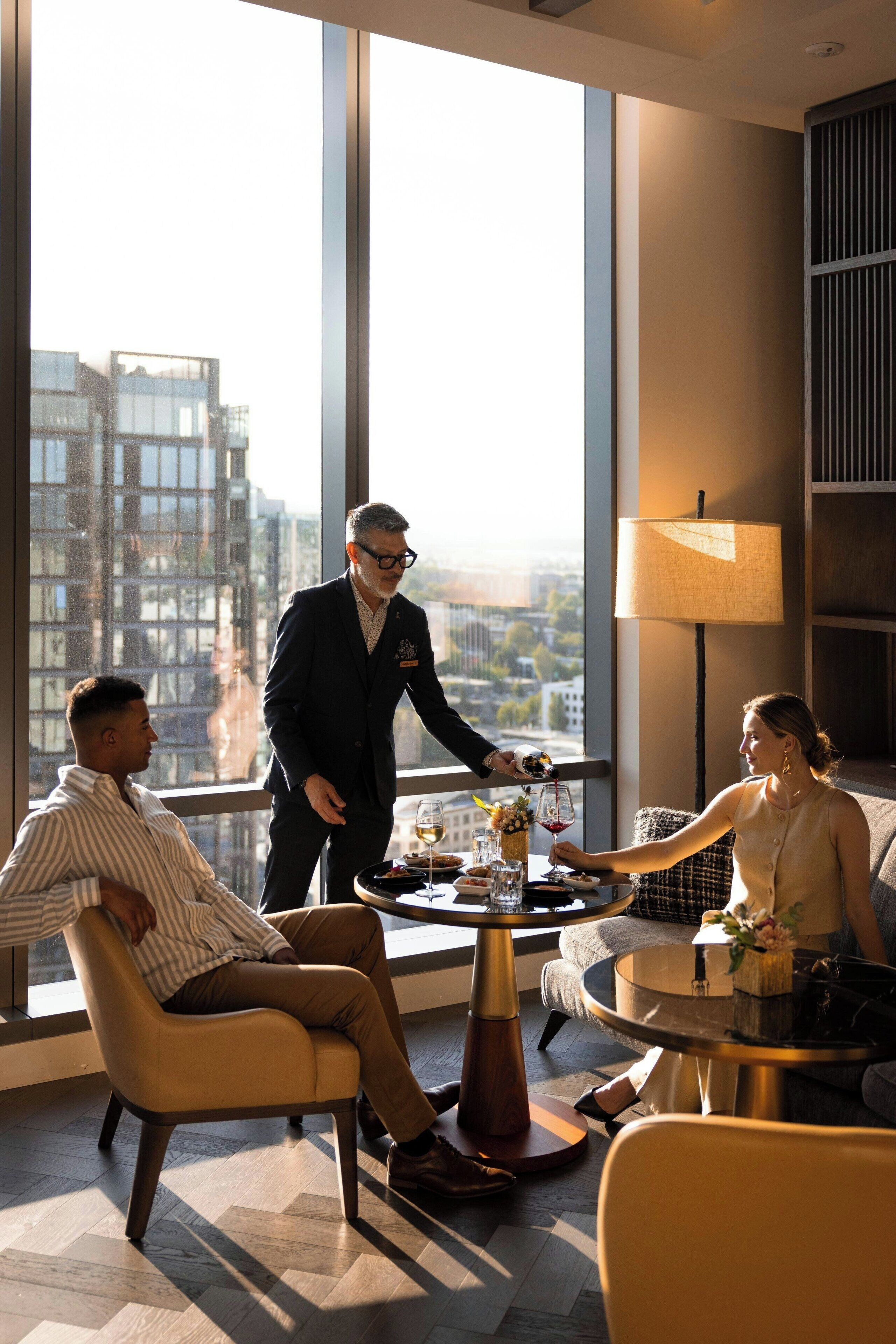 A modern hotel room with a large window, a round table, and a sofa.