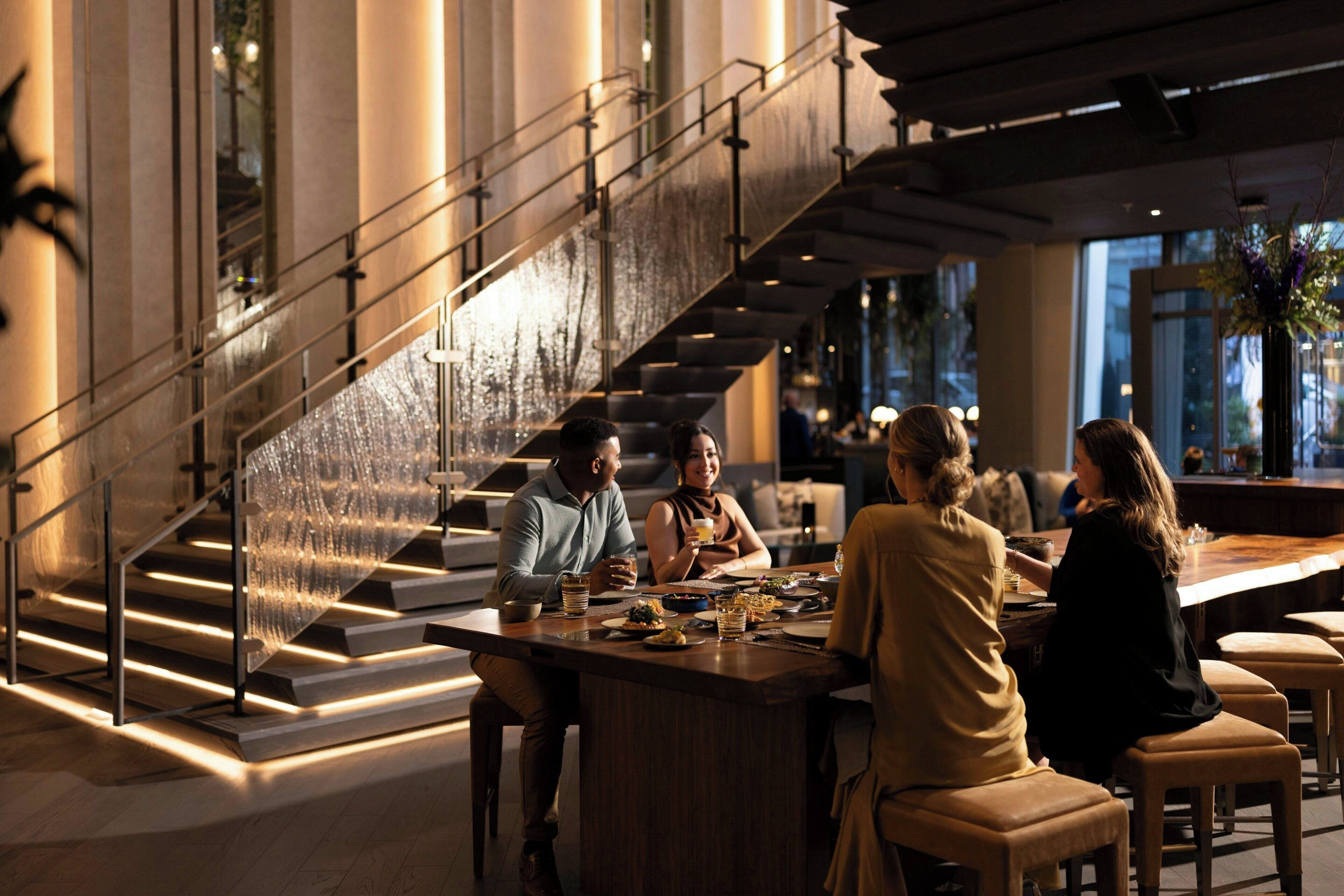 A modern interior with a staircase, a dining area, and large windows.