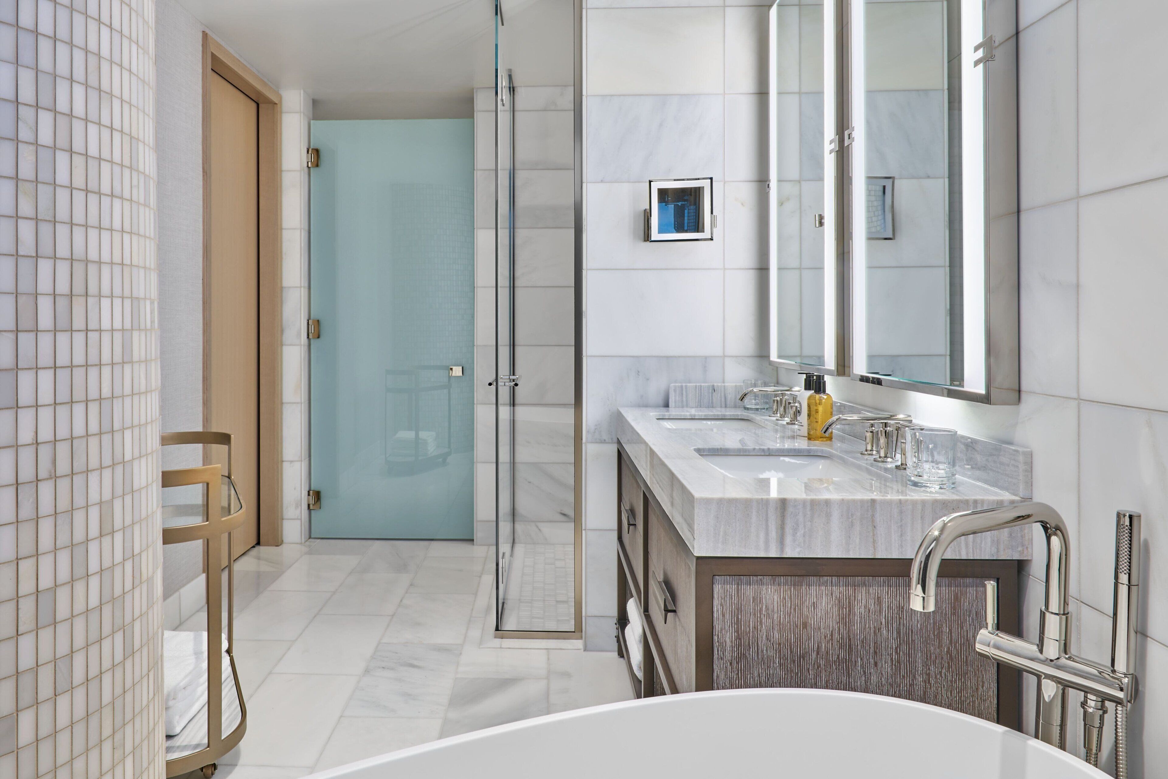 A modern bathroom with a large bathtub, two sinks, a glass shower enclosure, and a wooden vanity.