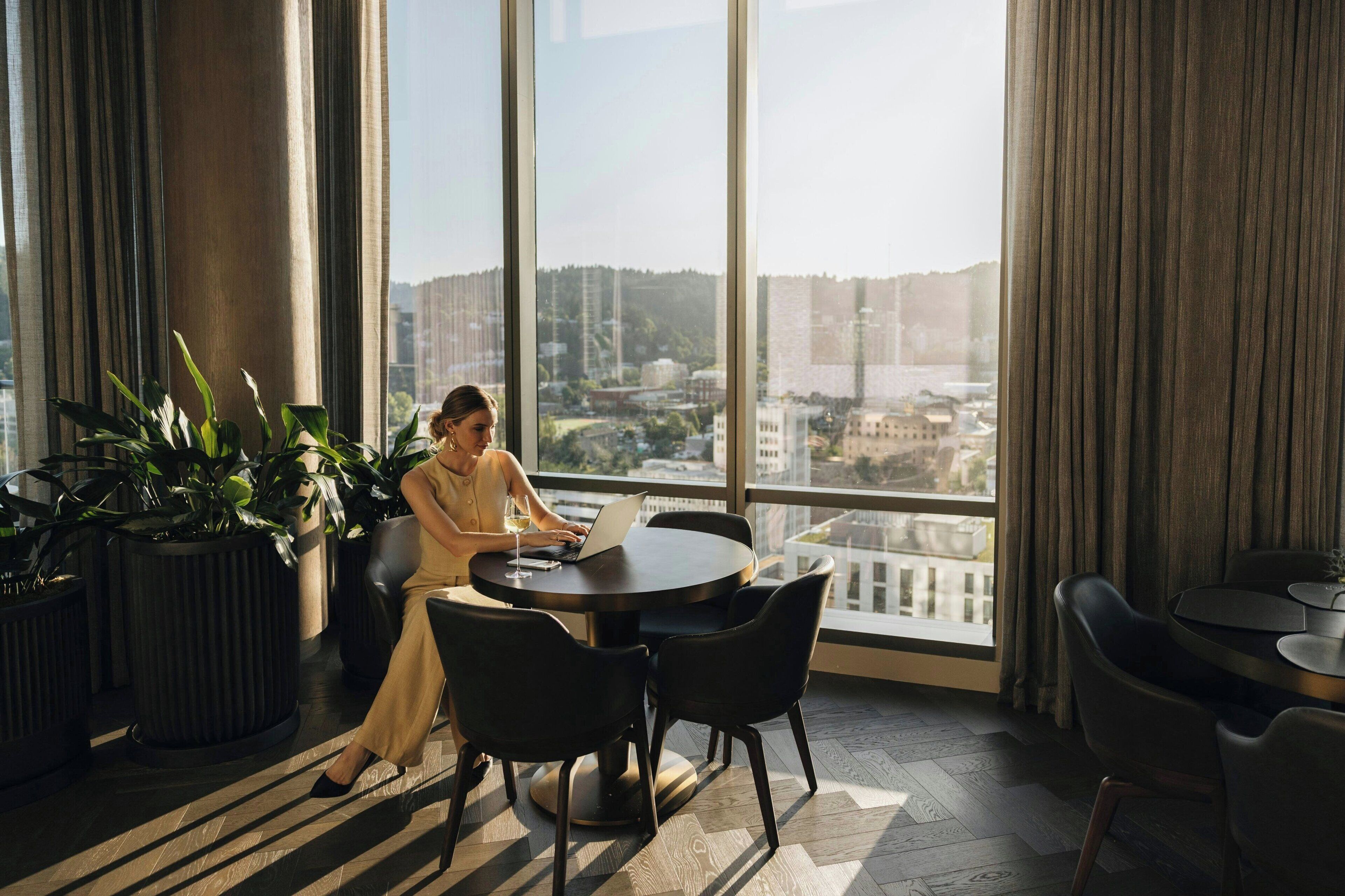 A modern hotel room with a large window, a round table, and several chairs.
