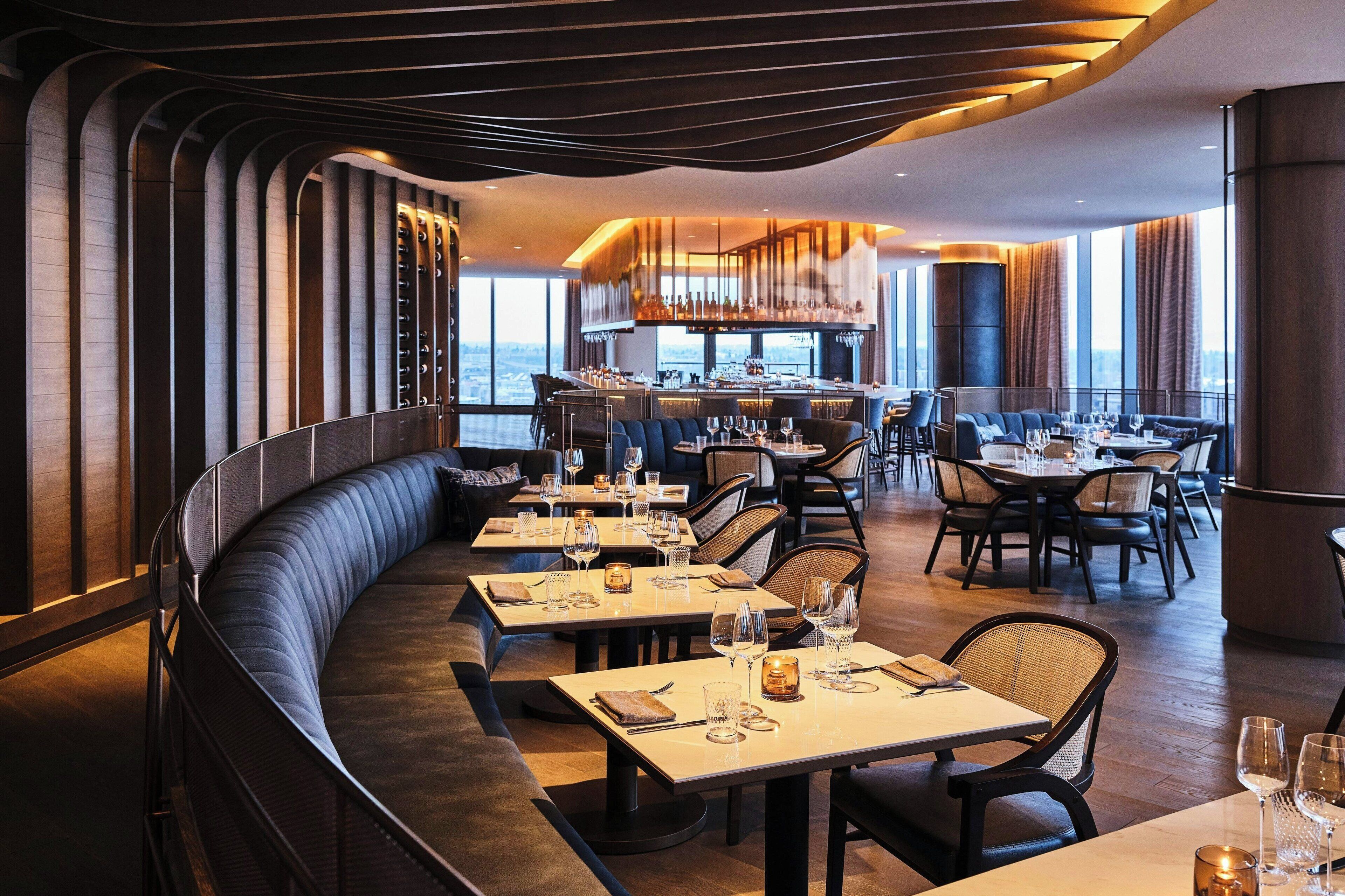 A modern restaurant with a curved seating area, a bar, and a view of the city.