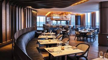 A modern restaurant with a curved seating area, a bar, and a view of the city.