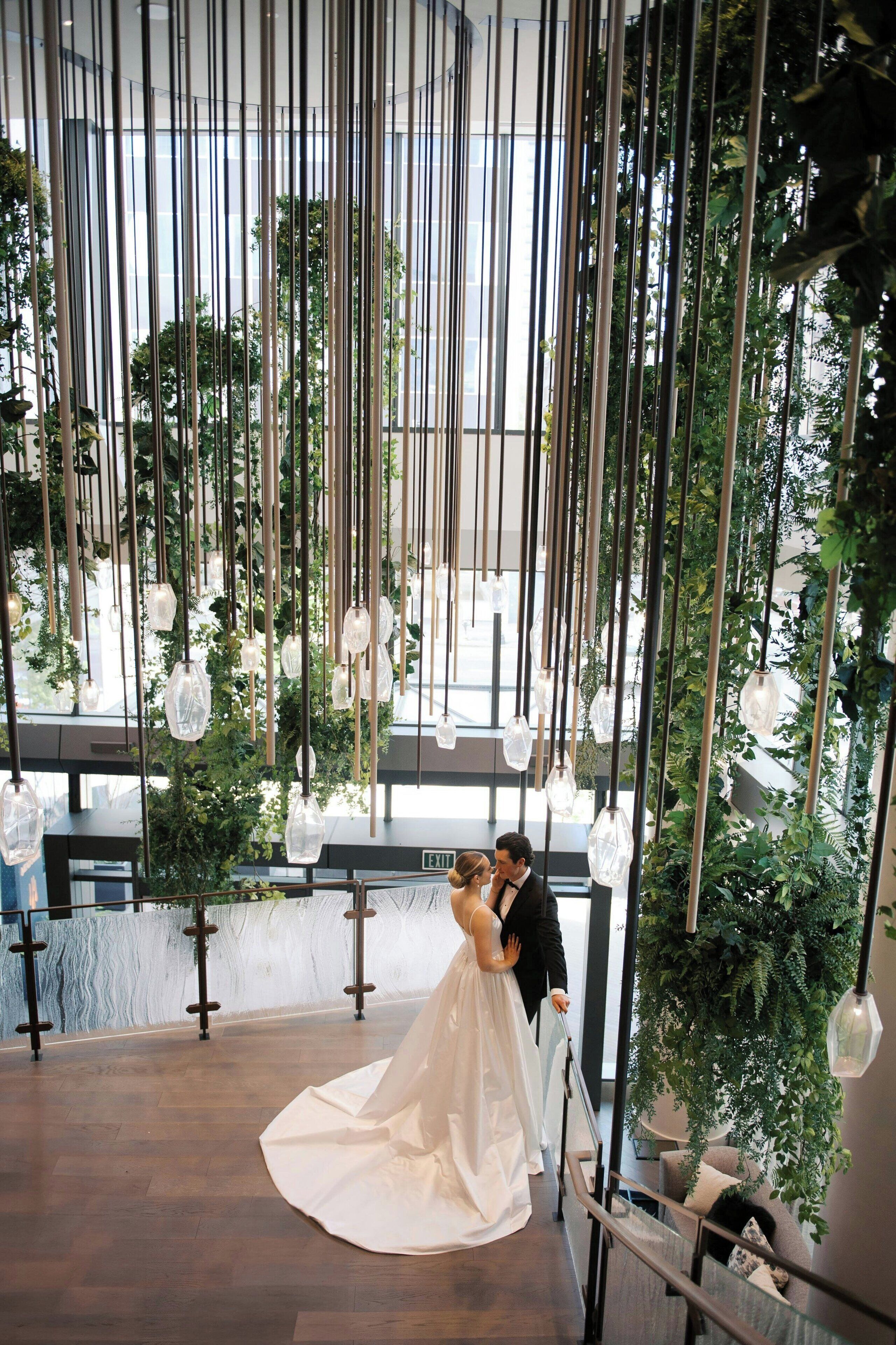 Un couple s'embrasse dans un intérieur moderne, agrémenté de luminaires suspendus et de plantes.