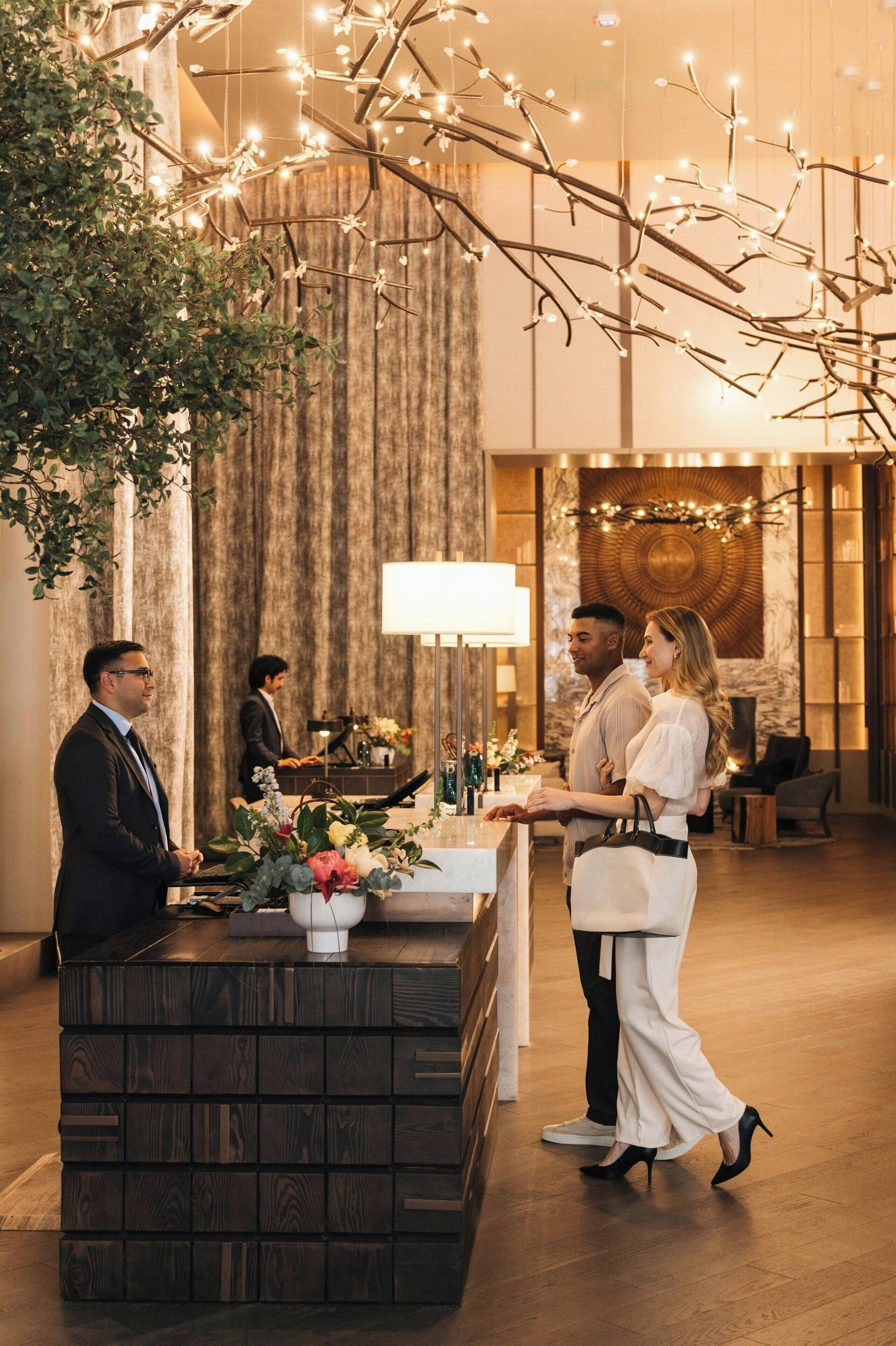 A reception area with a wooden reception desk, a large mirror, and a chandelier with hanging lights.