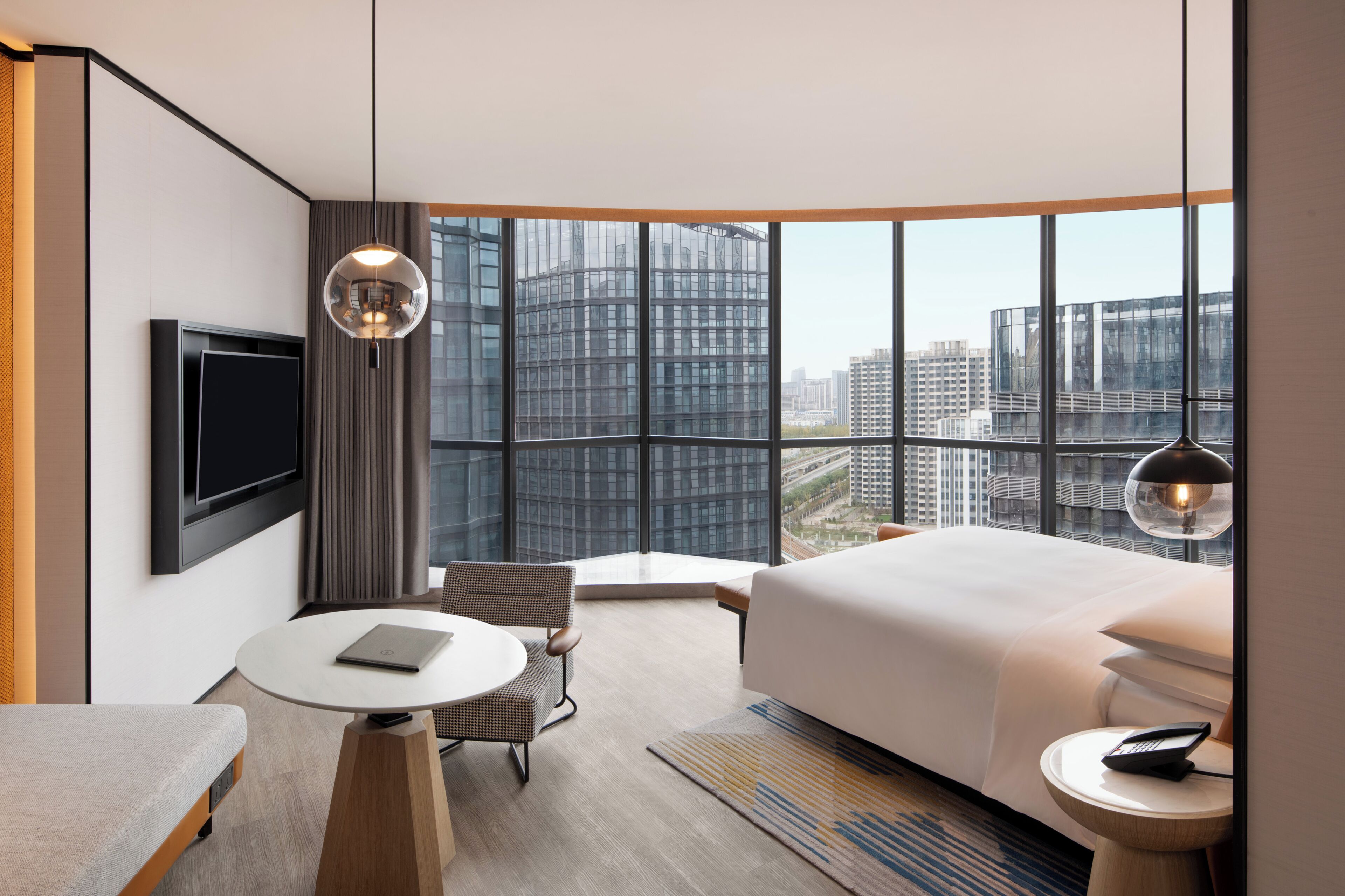Habitación de hotel moderna con una cama grande, un escritorio, una silla, un televisor y vistas a la ciudad.
