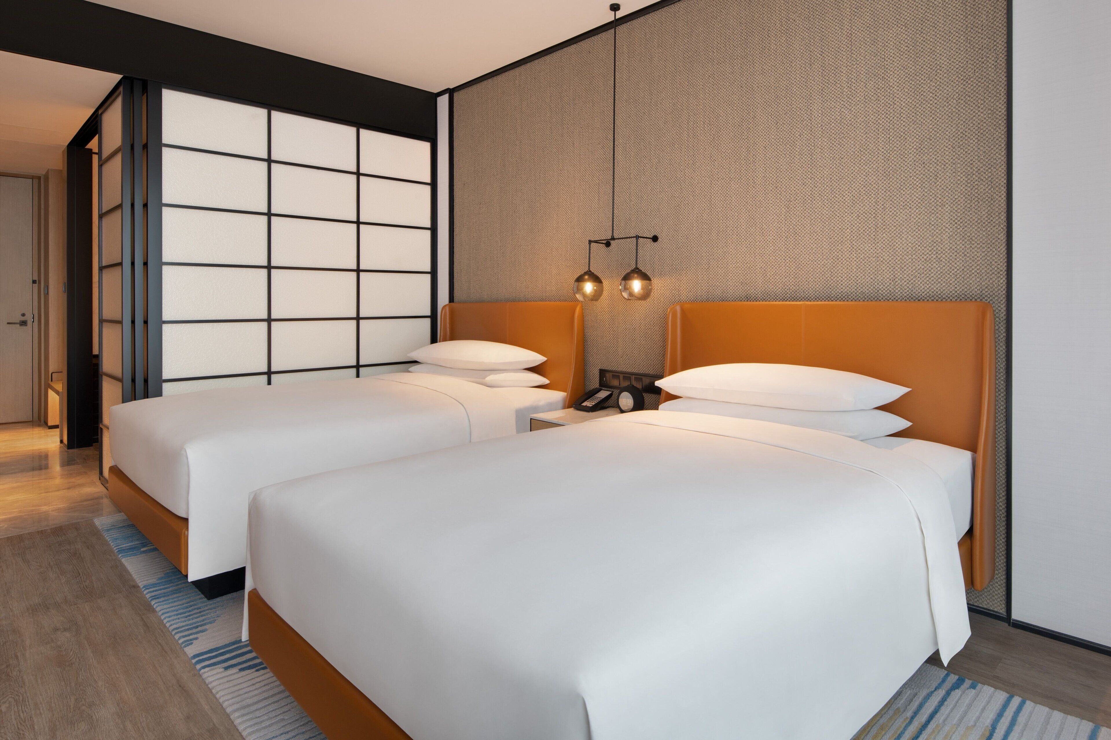 Quarto de hotel moderno com duas camas, uma janela grande e parede com textura.