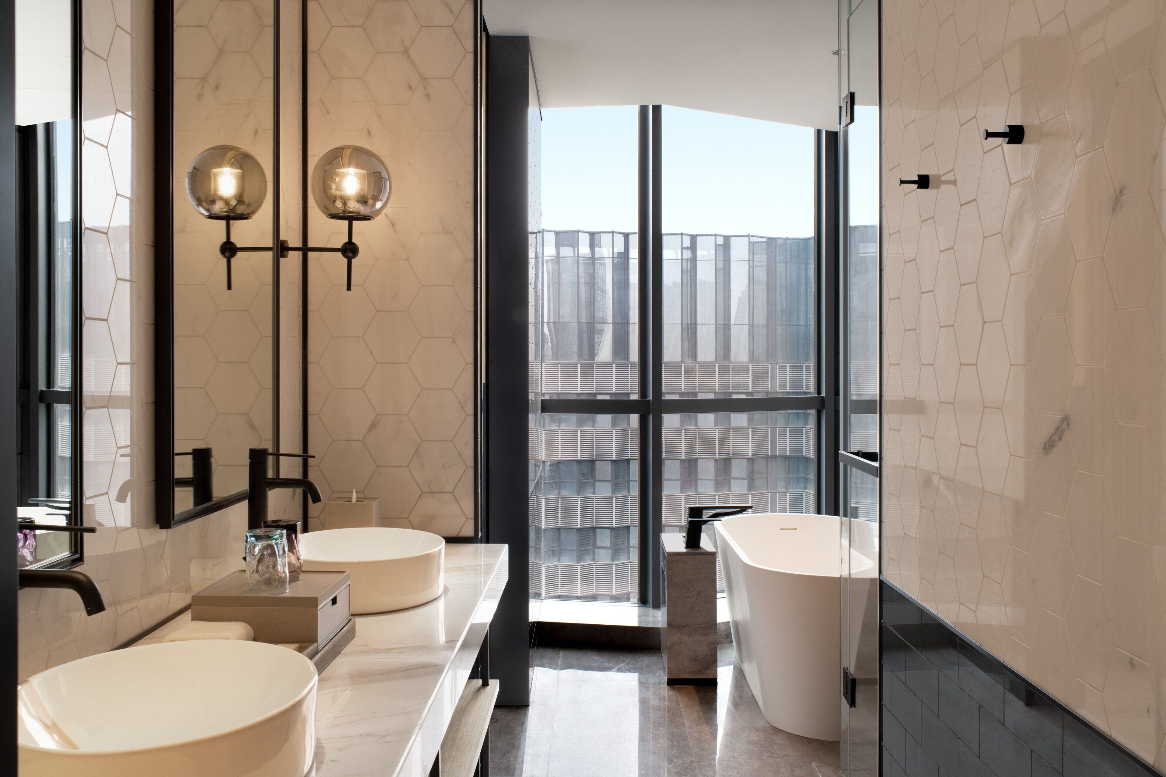 Un baño moderno con dos lavamanos redondos, un espejo grande y vistas de la ciudad a través de un ventanal.