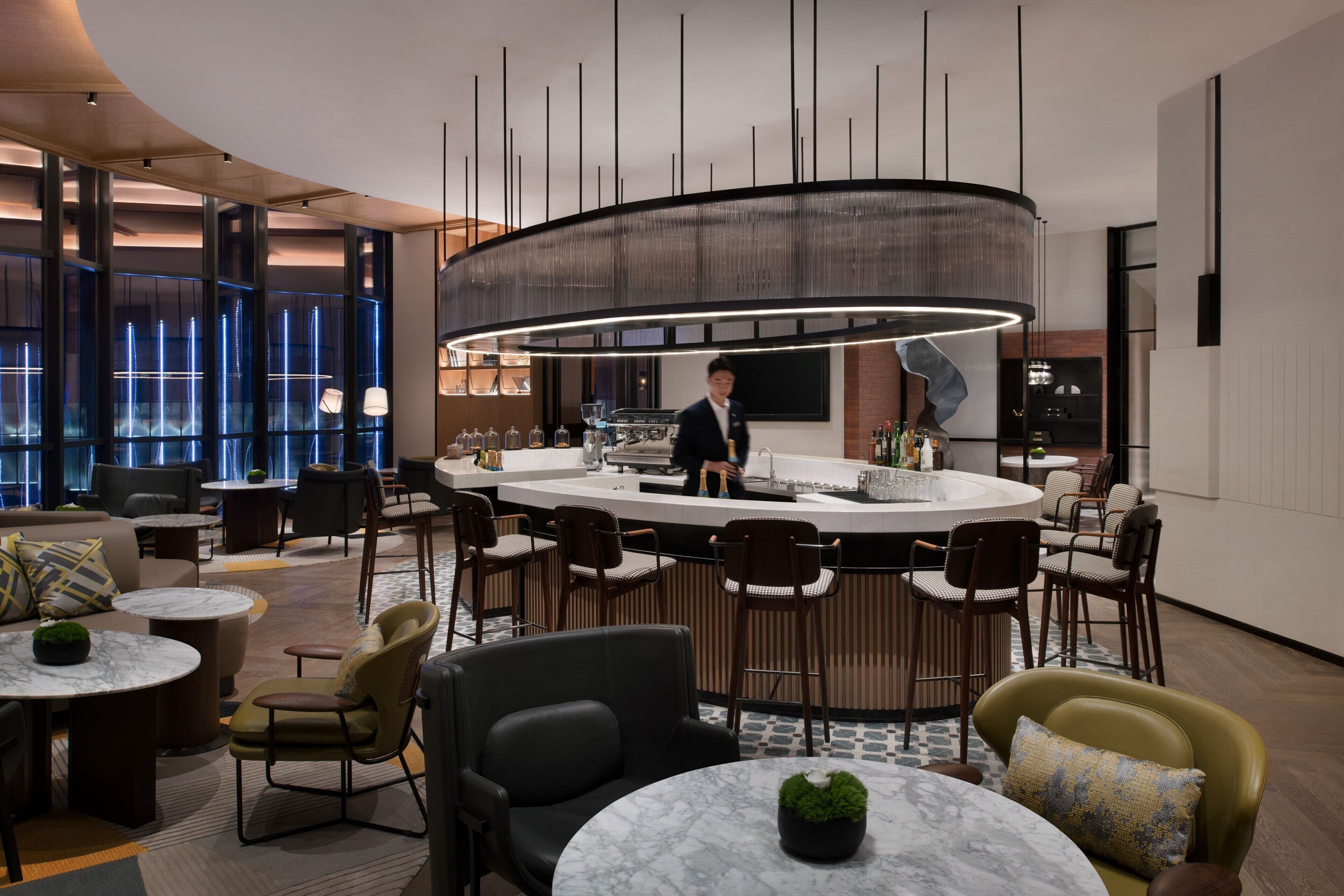 Un área de bar moderna con barra circular, asientos y un cantinero visible.