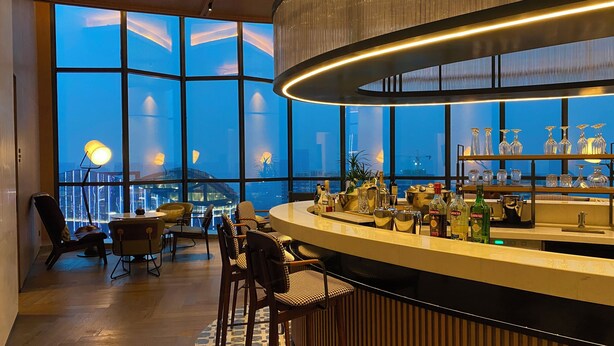 A modern bar with a curved counter, large windows, and a city view. - Sheraton Xi'An Chanba (Xi'an)