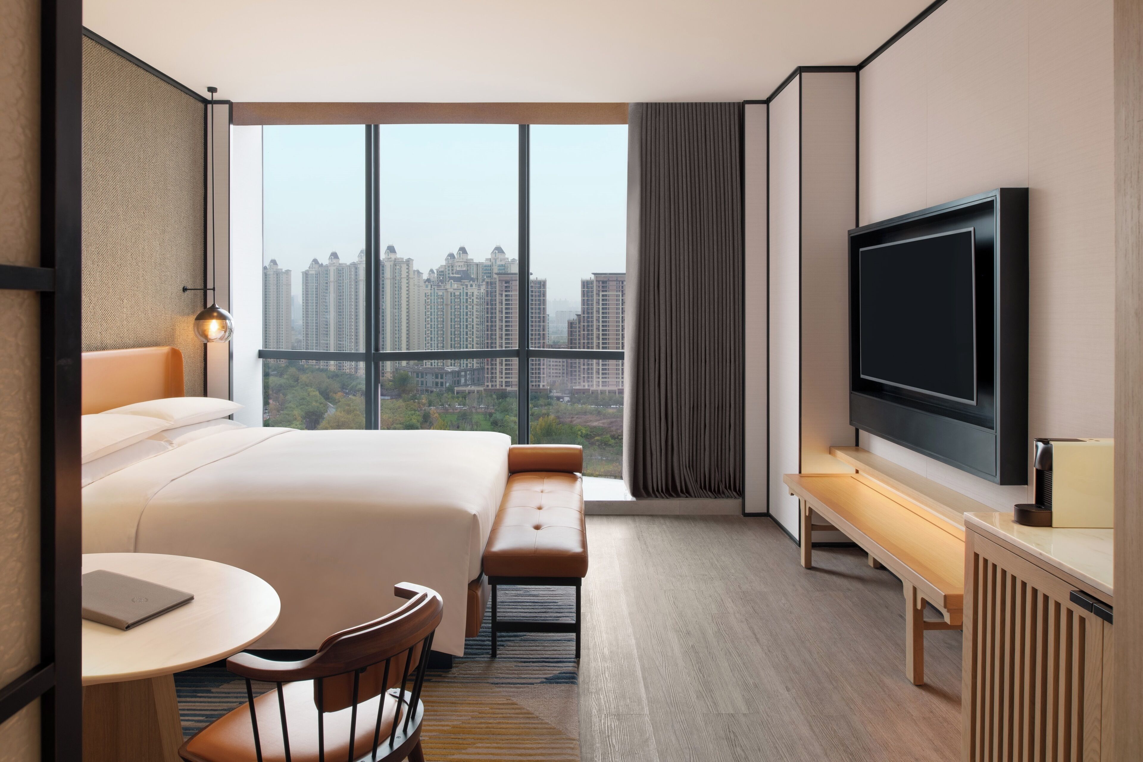 Een hotelkamer met een groot bed, een bureau met een laptop, een televisie en uitzicht op hoge gebouwen.