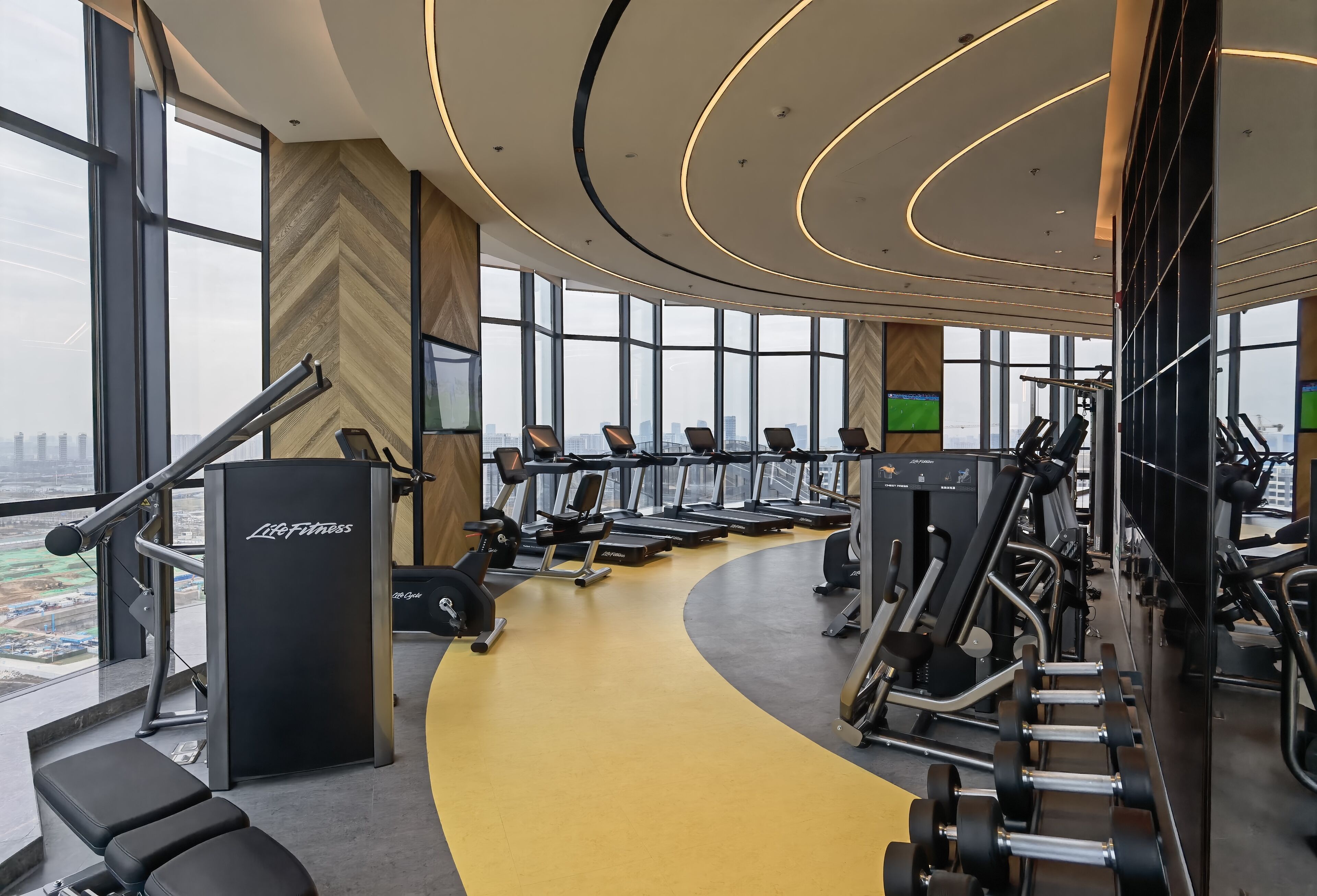 Un gimnasio moderno con máquinas de cardio, equipamiento de levantamiento de pesas y una pista de atletismo amarilla.